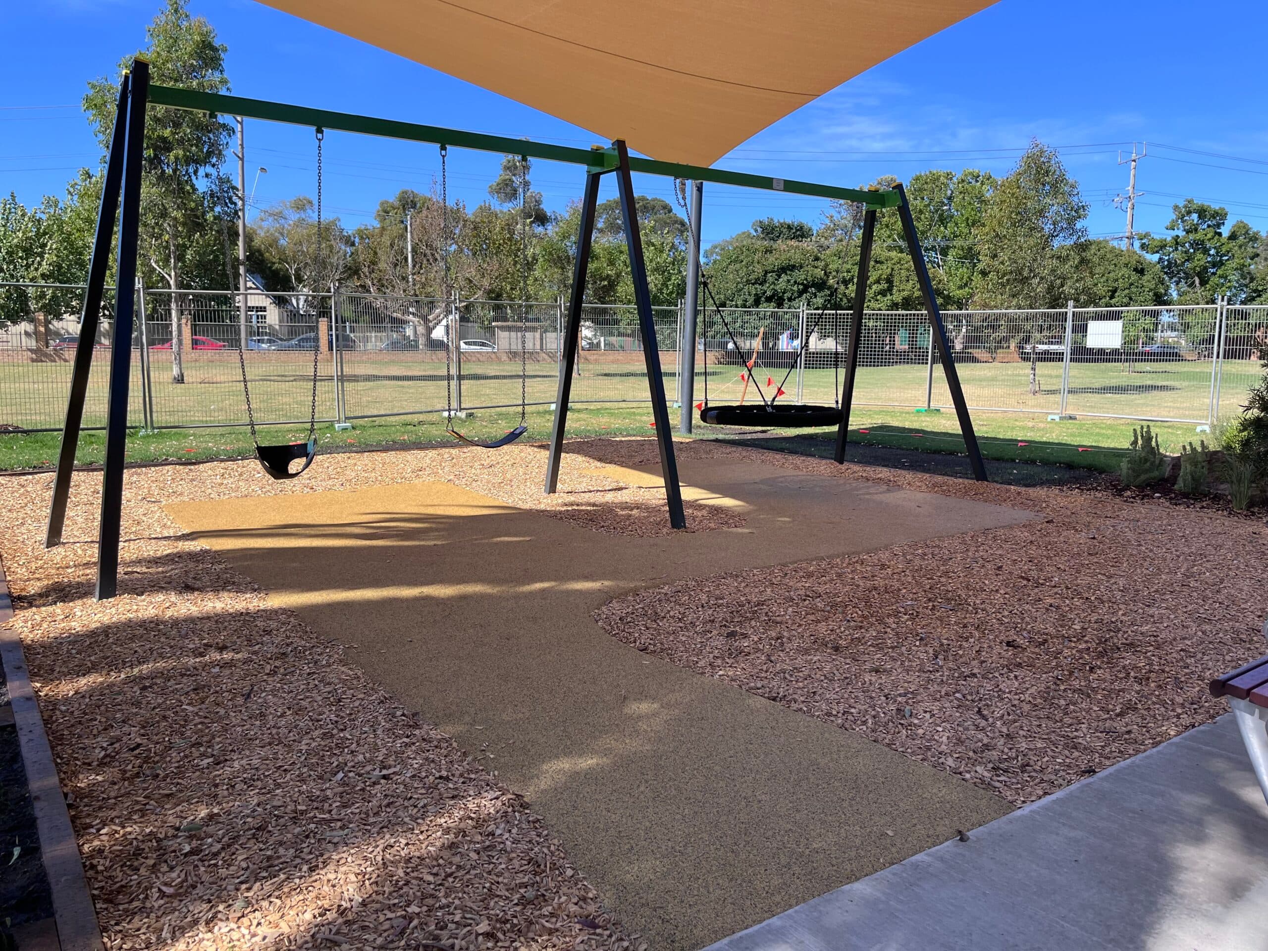Swings beneath a shade sail on mulched play surfacing